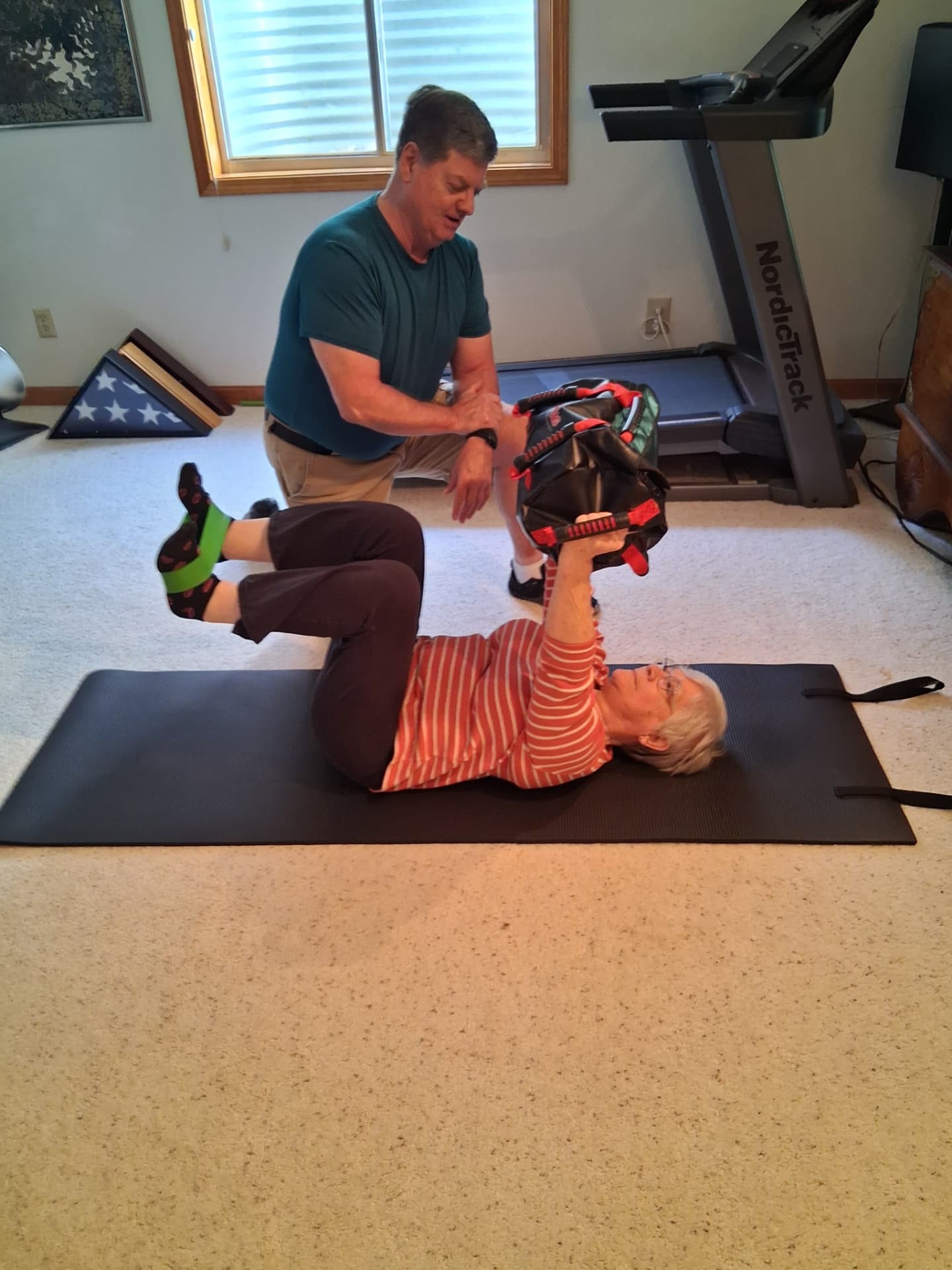 Jeff coaching an older client through a supported core exercise on a mat at home